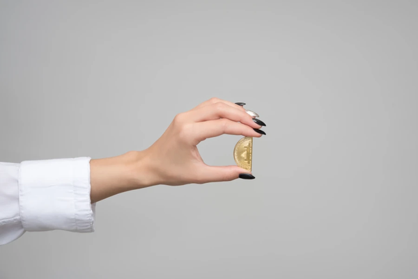 A hand holds a gold "Bitcoin" coin that has been cut in half
